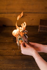 Hands holding burning banknotes against a wooden background, symbolizing financial waste.